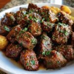 A plate of Garlic Butter Beef cubes garnished with fresh herbs, served with potatoes.