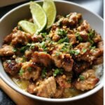 A bowl of Ginger Lime Pork with Coconut, garnished with fresh lime wedges and herbs.
