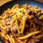 A close-up of High Protein Beef Pasta in a bowl, featuring pasta, beef, sauce, and melted cheese, garnished with parsley.