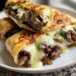 Two Keto Philly Cheesesteak Rolls stacked on a white plate, filled with steak and melted cheese.