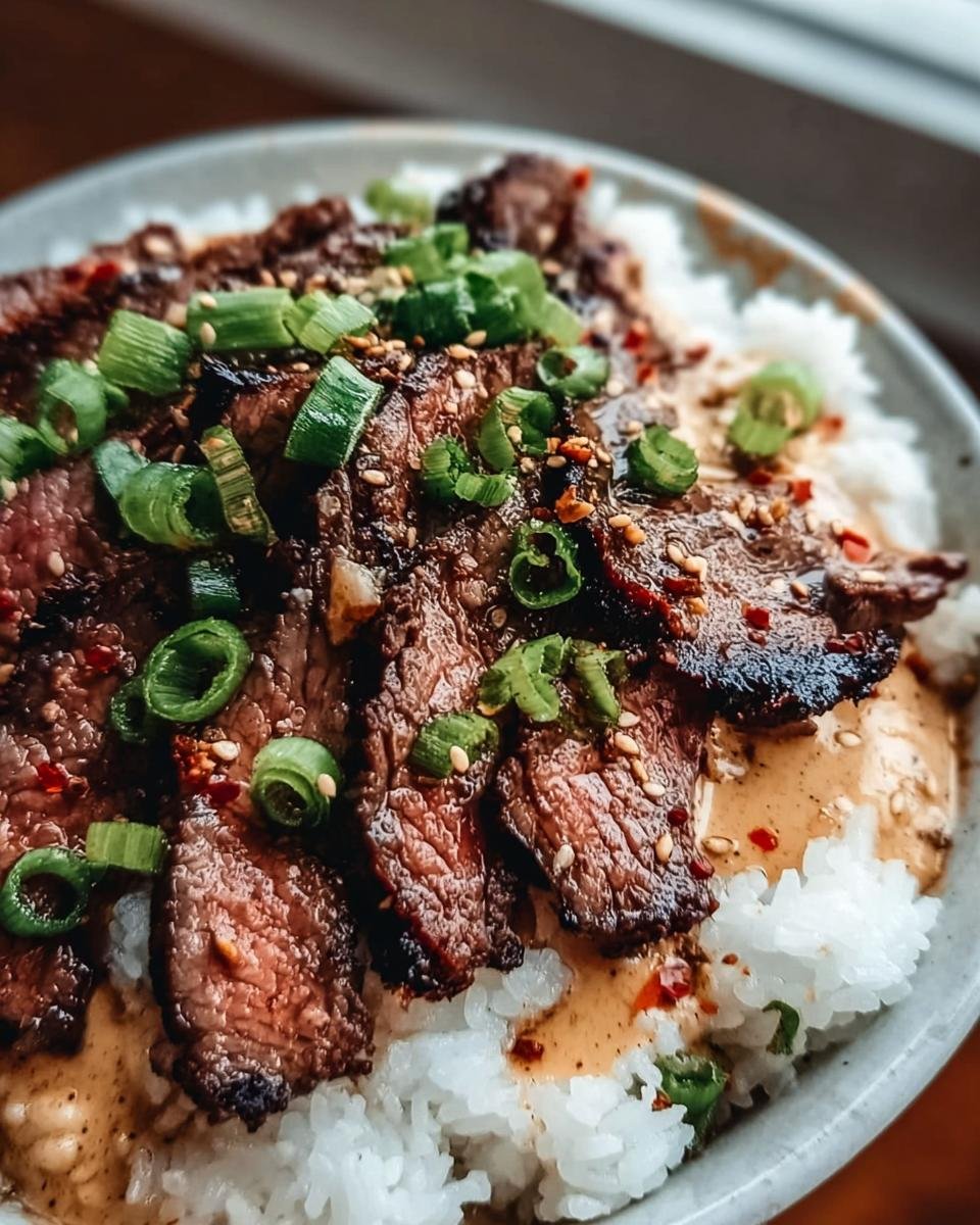 A close-up of Korean BBQ Steak Rice bowl with sliced steak, rice, sauce, and green onion garnish.