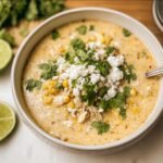 A bowl of creamy Mexican Street Corn Soup topped with cotija cheese and cilantro. Lime wedges on the side.