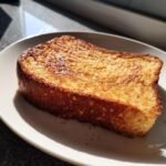 Single slice of golden brown 40 g Protein French toast on a white plate, lit by sunlight.