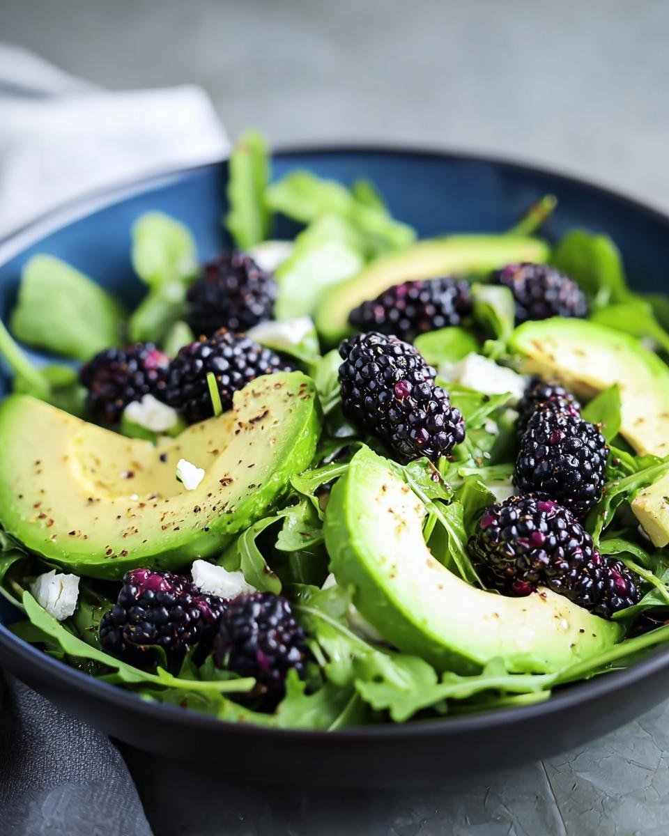Close-up of a Blackberry, Avocado & Arugula Salad in a blue bowl. Fresh and vibrant salad.