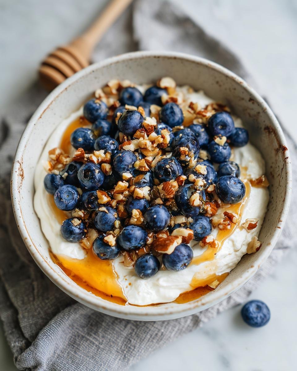 A bowl of Blueberry Cottage Cheese Breakfast topped with blueberries, nuts, and honey.