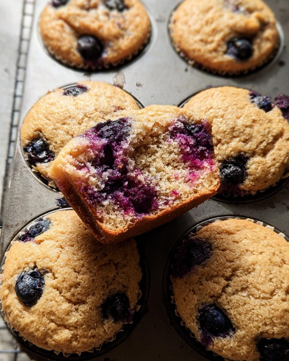 Close-up of Blueberry Protein Muffins in a muffin tin, one muffin cut in half to show the inside.
