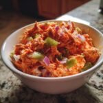 A bowl of Buffalo Chicken Salad with shredded chicken, celery, and red onion on a marble countertop.