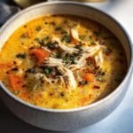 Close-up of a bowl of Cajun Chicken Soup with shredded chicken, carrots, and herbs.