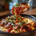 Spoon lifting a portion of Chicken Parm Cottage Bowl, showcasing melted cheese and tomato sauce.