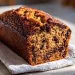 A full loaf of Chocolate Espresso Banana Bread, studded with chocolate chips, sits on a linen cloth.