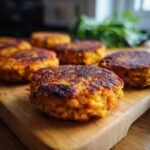 Several crispy sweet potato lentil patties arranged on a wooden cutting board with fresh greens in the background.