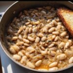 Overhead shot of French Onion White Beans in a pan, served with a slice of toasted bread.