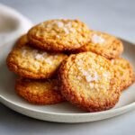 A stack of golden brown French Salted Butter Cookies sprinkled with coarse salt on a speckled plate.