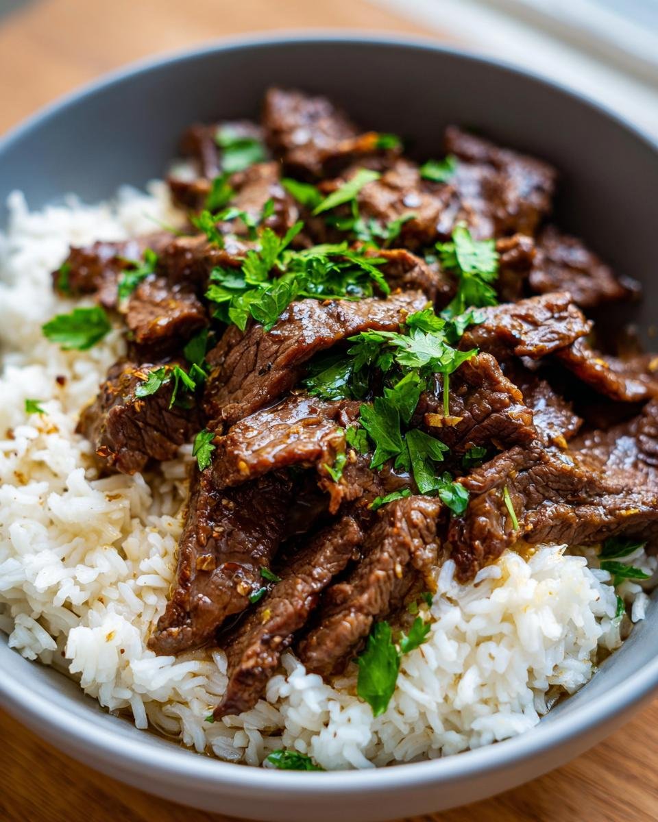 Close-up of Garlic Butter Beef and Rice in a bowl, garnished with fresh parsley.