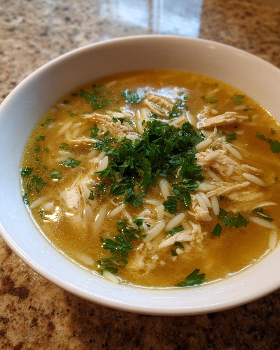 A bowl of Lemon Chicken Soup with shredded chicken, orzo pasta, and fresh parsley.