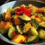 Close-up of a vibrant Mango Cucumber Salad in a bowl, garnished with red chili peppers and herbs.