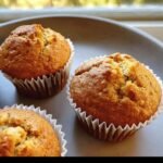 Three freshly baked muffins with Greek yogurt in white paper liners, arranged on a grey plate.
