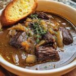 Close-up of a bowl of Onion Beef Short Soup with a slice of toasted bread and fresh thyme.