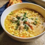 A comforting bowl of Penicillin Soup with noodles, chicken, vegetables, and fresh herbs.