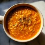 Overhead shot of a mug filled with creamy Pumpkin Wild Rice Soup, garnished with herbs.