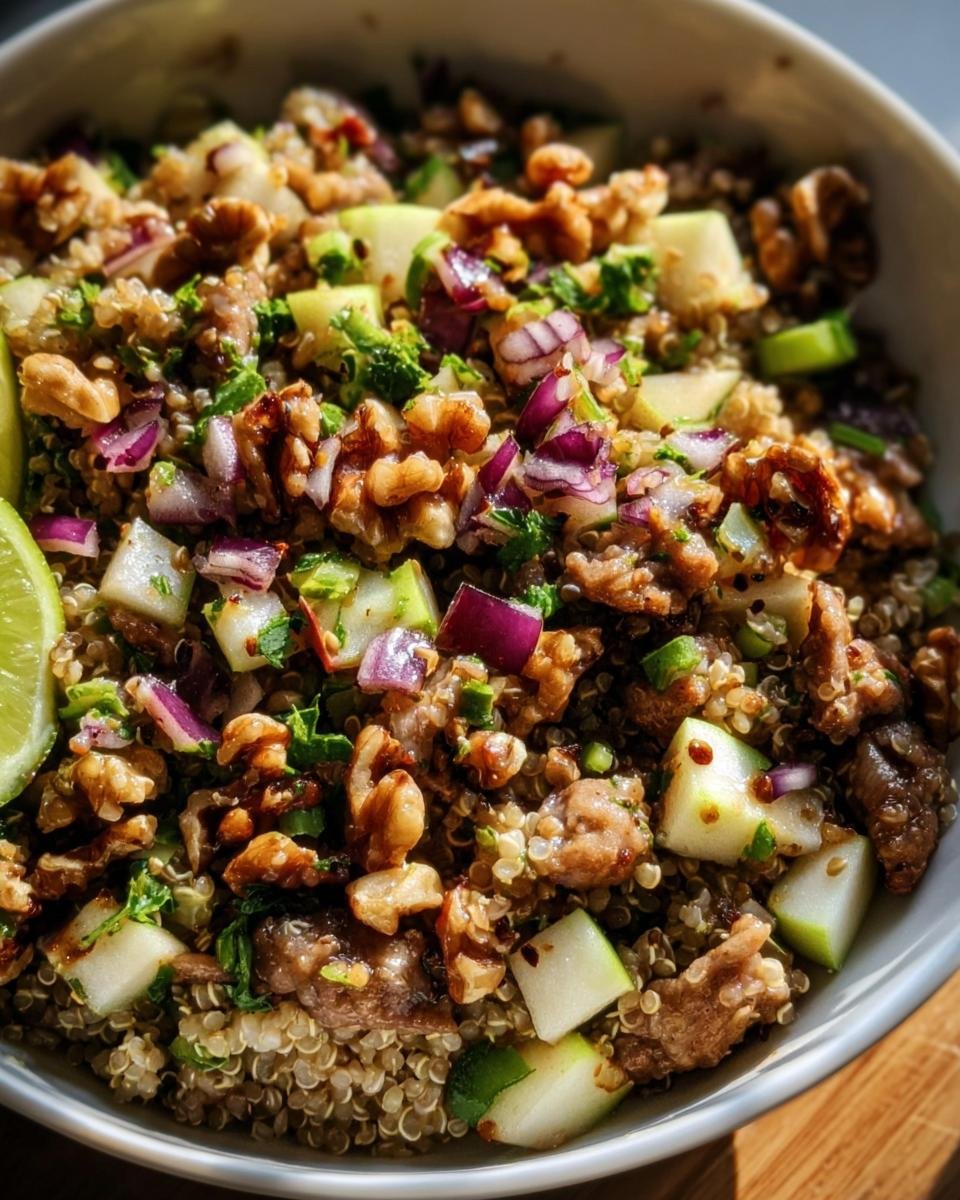 Close-up of a Quinoa Apple Salad in a bowl with quinoa, apples, walnuts, red onion, herbs, and a lime wedge.