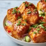 Close-up of glazed Salmon Bites Bowls served over rice with fresh cucumber, peppers, and green onions.