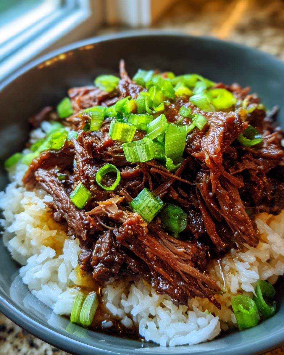 Bowl of Slow Roast Asian Beef served over rice, garnished with fresh green onions.