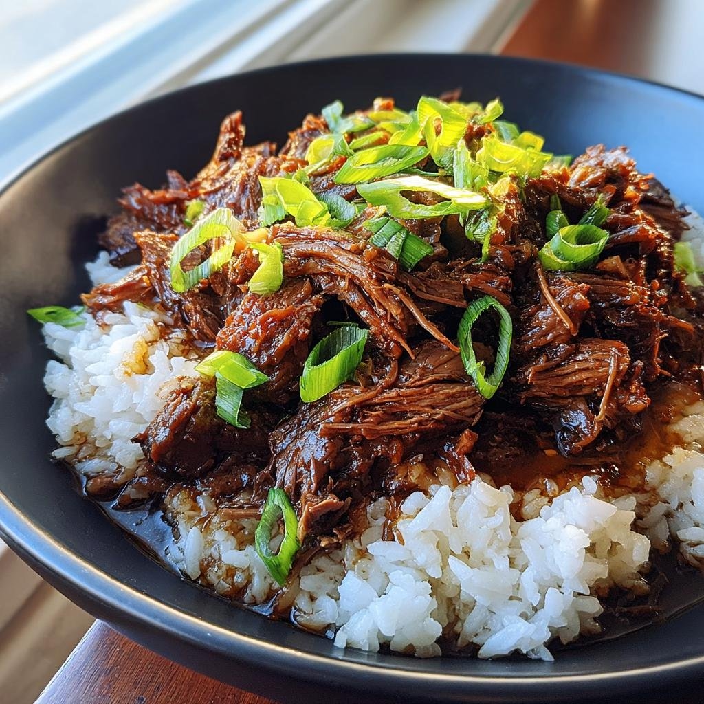 A bowl of Slow Roast Asian Beef served over rice and garnished with fresh green onions.