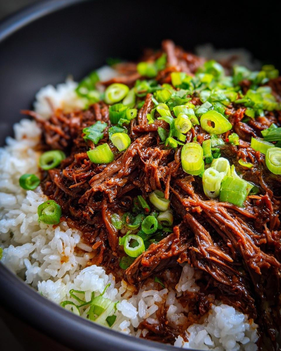Close-up of Slow Roast Asian Beef served over white rice and garnished with fresh green onions.