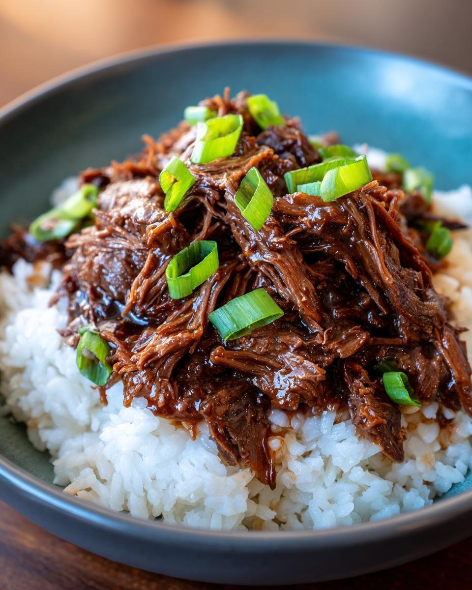 A bowl of Slow Roast Asian Beef served over white rice, garnished with fresh scallions.
