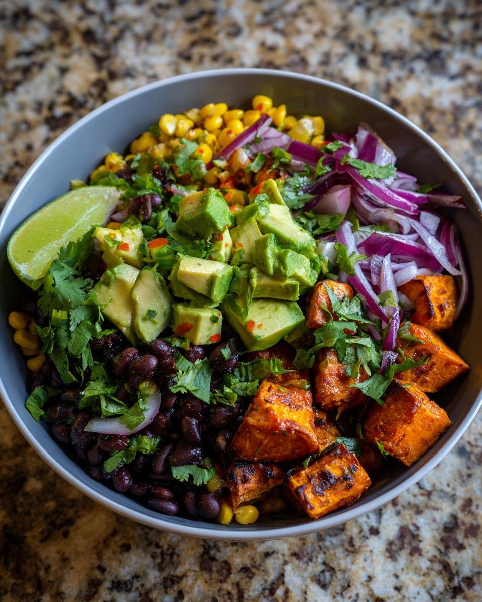 A vibrant Sweet Potato Bowls featuring roasted sweet potatoes, black beans, corn, avocado, red onion, and a lime wedge.