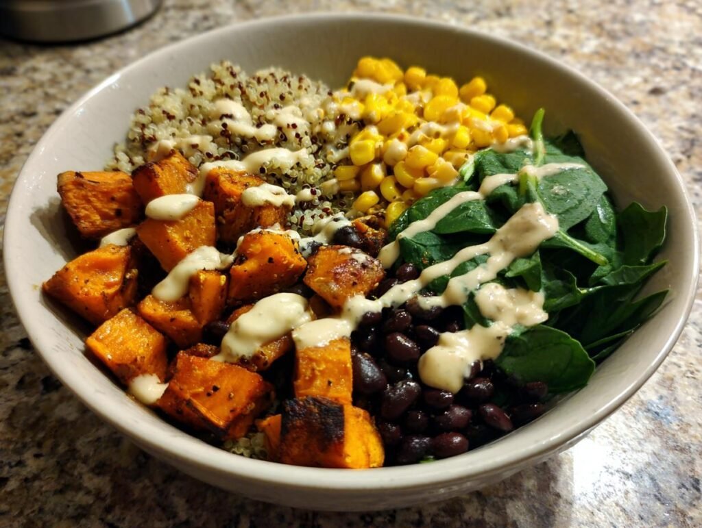 A vibrant Sweet Potato Buddha Bowl with roasted sweet potatoes, quinoa, corn, black beans, spinach, and tahini dressing.