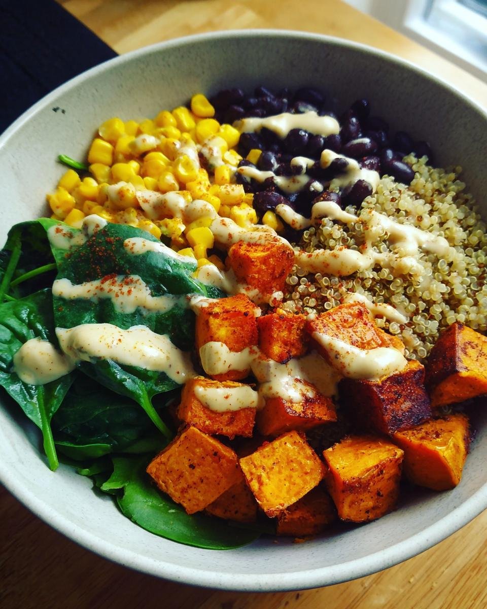 A vibrant Sweet Potato Buddha Bowl with corn, black beans, quinoa, spinach, and a creamy dressing.
