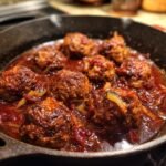 Close-up of Tender Red Wine Meatballs simmering in a cast iron skillet with a rich sauce.