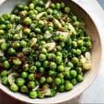 Bowl of vibrant green Thanksgiving Peas with onions, herbs, and bacon bits.