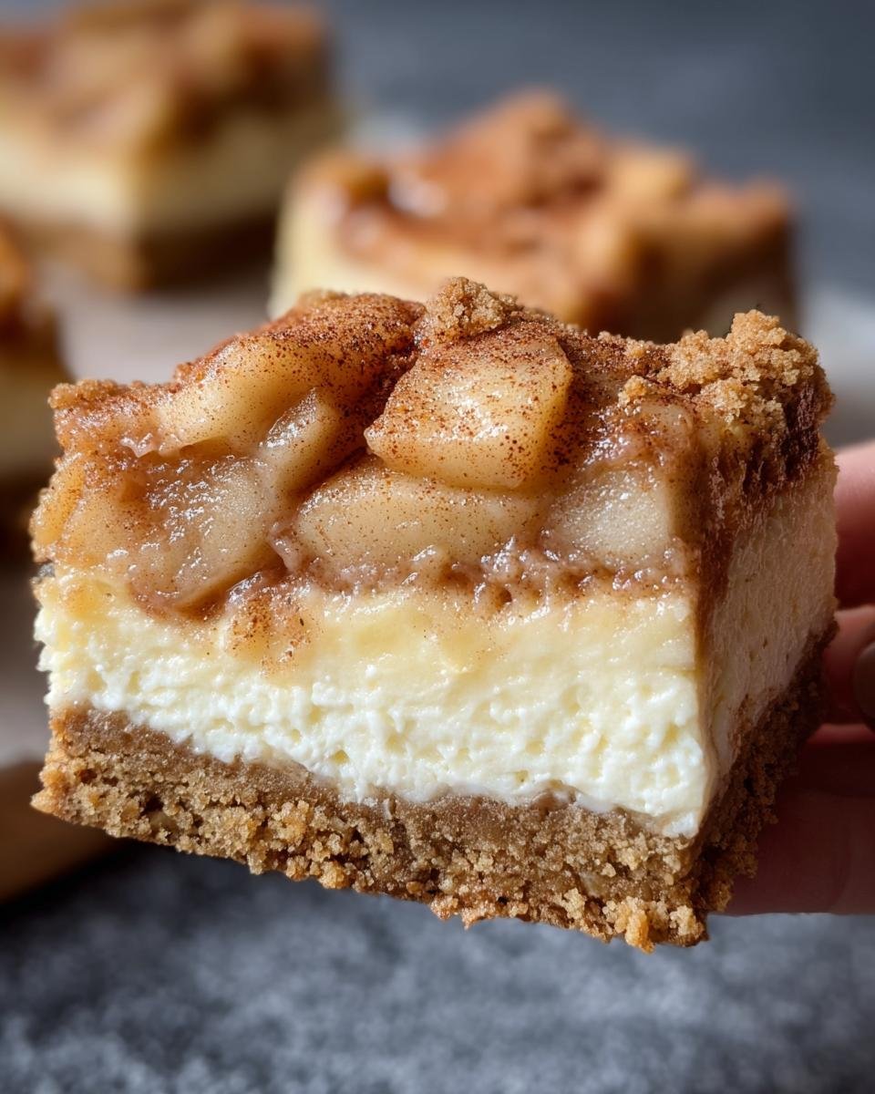 A close-up of a slice of Apple Pie Cheesecake Bars, showcasing layers of crust, cheesecake, and apple pie filling.