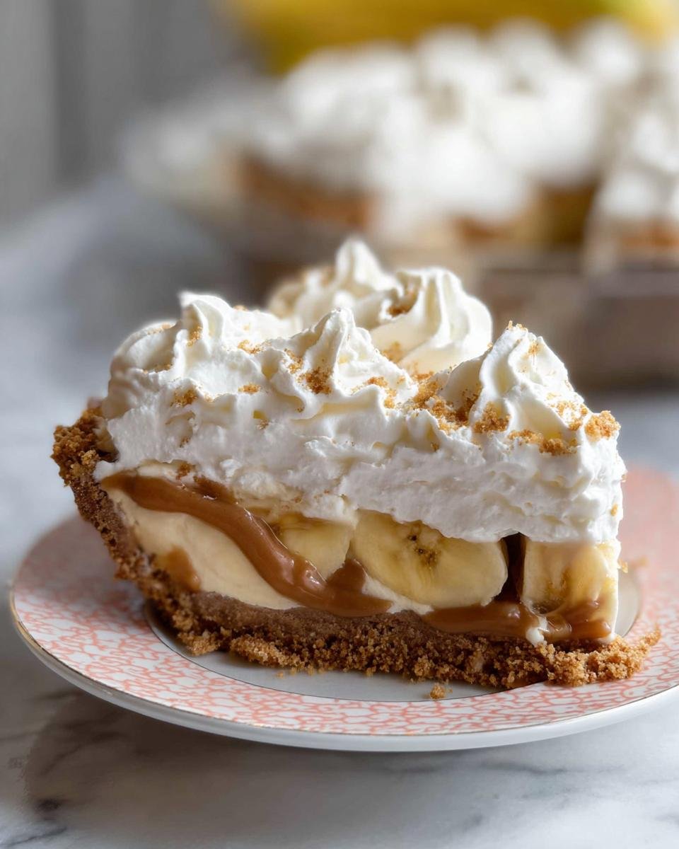 A thick slice of Banoffee Pie with whipped cream, bananas, and caramel on a patterned plate.