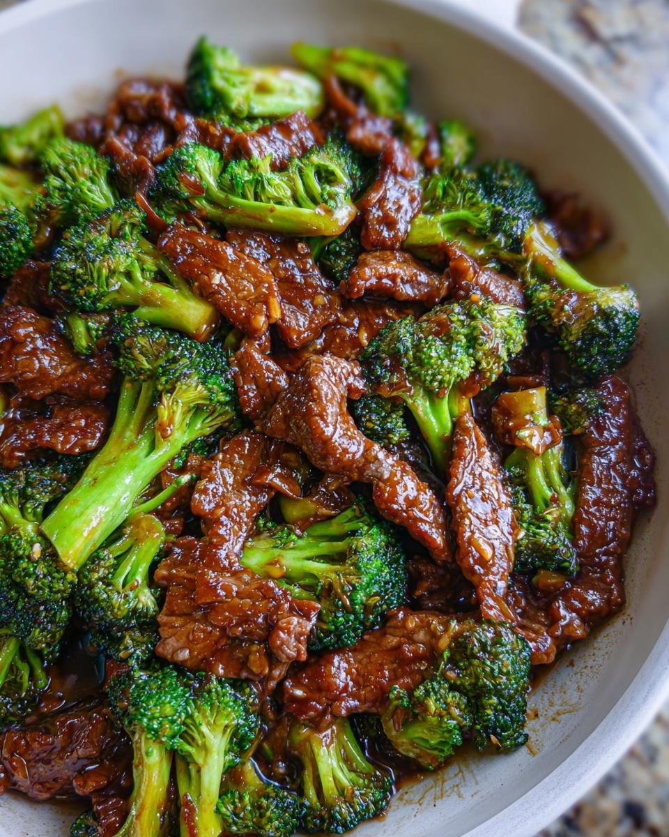Close-up shot of glossy, saucy Chinese Beef and Broccoli ready to eat in a white serving bowl.