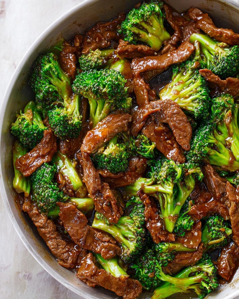 Close-up of vibrant Chinese Beef and Broccoli stir-fry coated in savory brown sauce in a metal pan.