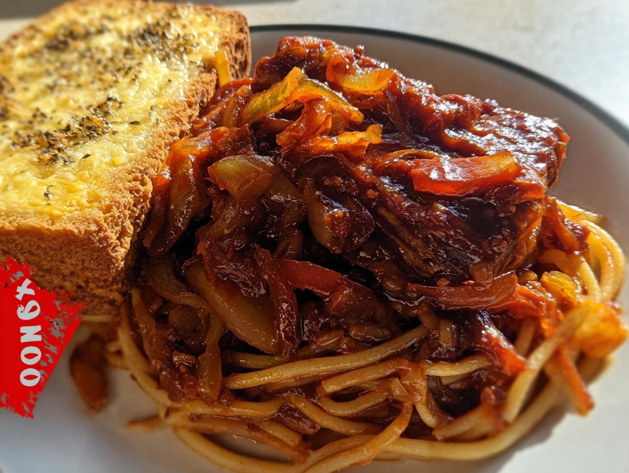 A serving of saucy leftover ribs meat and onions served over spaghetti noodles with a side of garlic bread, demonstrating one of the Best Leftover Ribs Recipes.