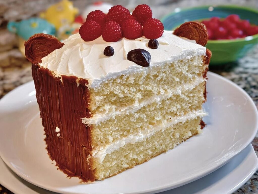 A slice of a fun bear-themed birthday cake, decorated with frosting, raspberries, and cookie ears.