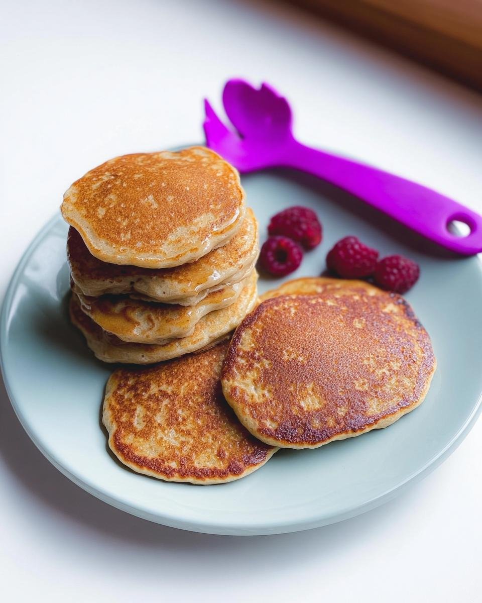 A stack of golden brown Three Ingredient Banana Pancakes served on a light blue plate with fresh raspberries.