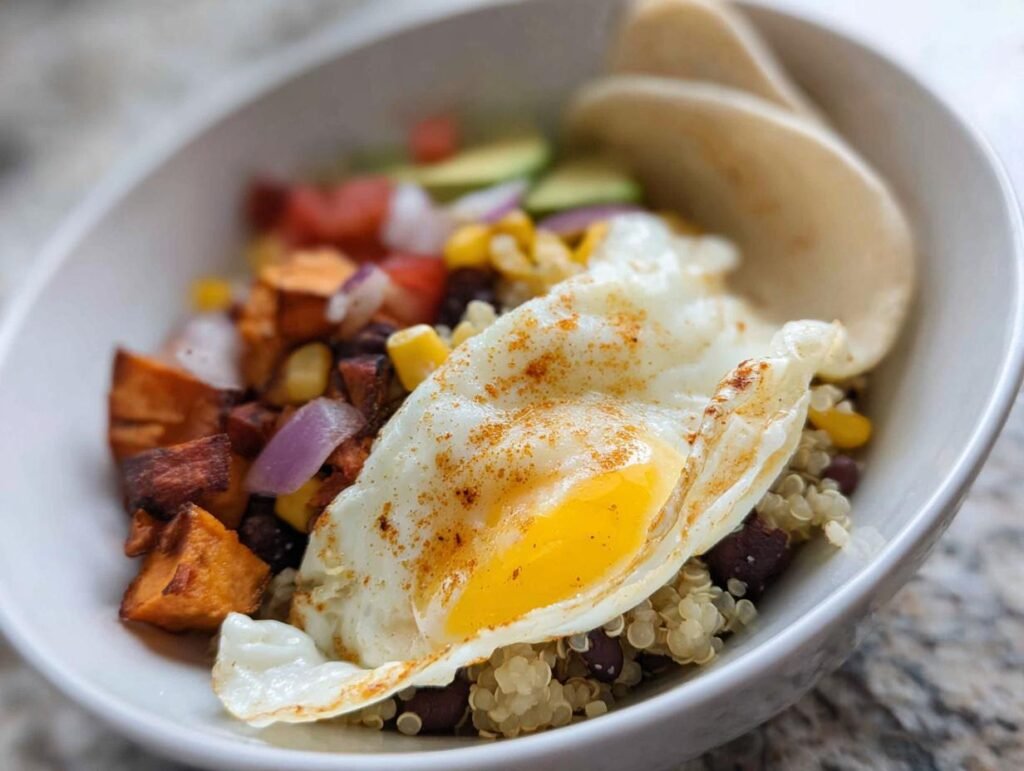 A vibrant Healthy Breakfast Burrito Bowl topped with a perfectly fried egg, sweet potatoes, black beans, corn, and avocado.