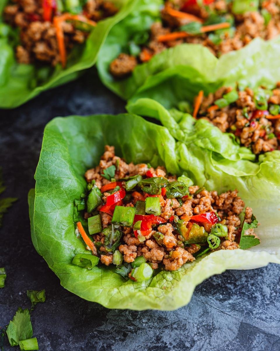Close-up of Healthy Turkey Lettuce Wraps filled with seasoned ground turkey, chopped peppers, carrots, and green onions.